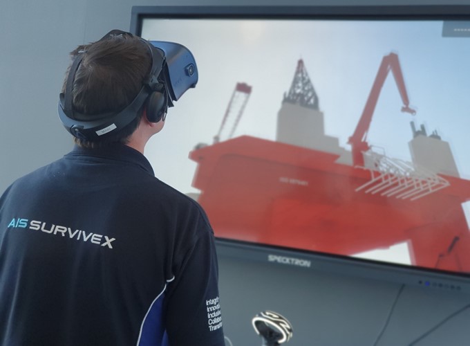 A person wearing a VR headset interacts with a virtual simulation of an offshore rig displayed on a large screen.