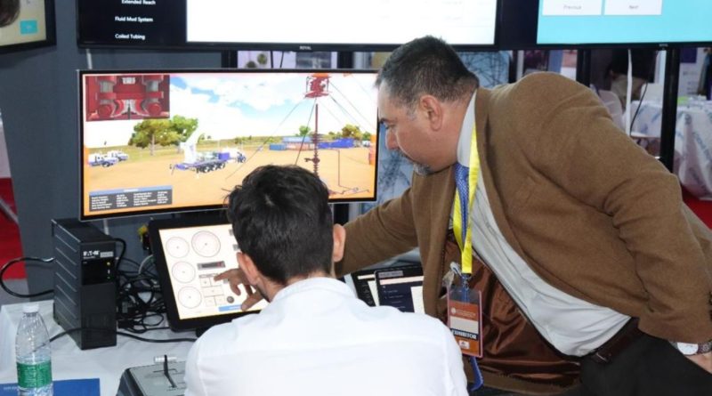 Two men interact with a control panel and monitor display in an industrial booth setting, demonstrating equipment operation.