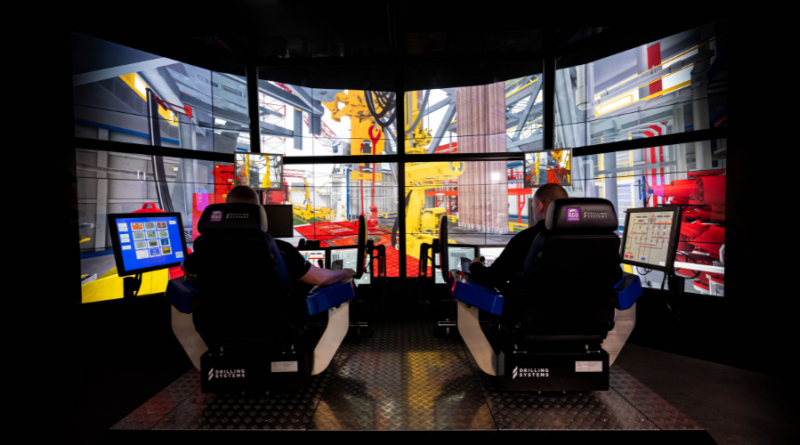 Two people seated in simulator chairs facing multiple screens displaying a construction site environment, with control panels in front of them.