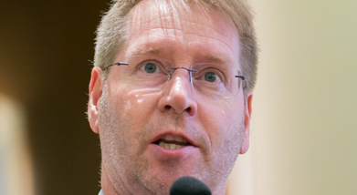 A man with glasses and a short beard speaks into a microphone.