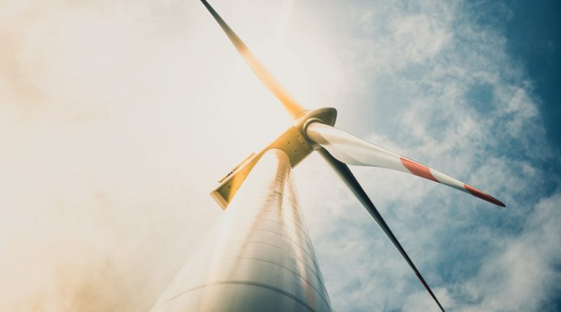Low-angle view of a wind turbine against a cloudy sky with sunlight illuminating the blade tips.