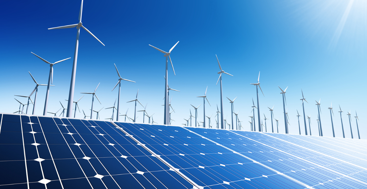 A large field of solar panels is placed in the foreground, with numerous wind turbines standing behind them under a clear blue sky. Both forms of renewable energy are depicted in the image.
