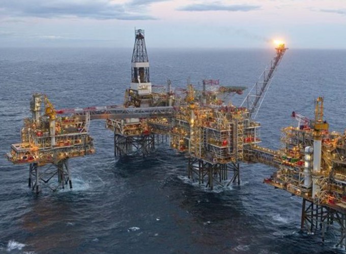 An offshore oil platform with multiple interconnected structures, surrounded by ocean water, under a partly cloudy sky.