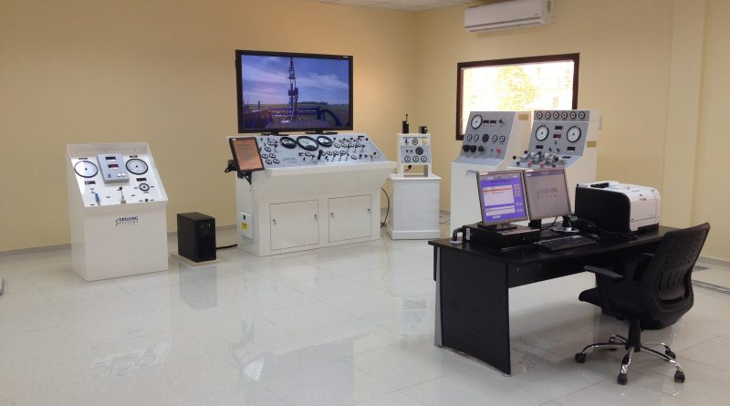 A control room with multiple consoles, a computer workstation, and large screens displaying data. Equipment includes dials, gauges, and control panels, all organized in a spacious, well-lit environment.