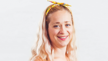 A woman with long blonde hair, wearing a yellow headband, smiles in front of a plain white background.
