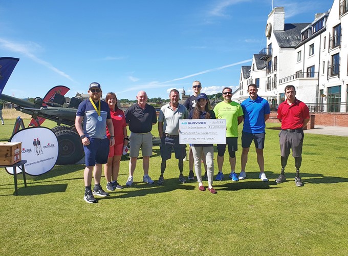 A group of people stand on a golf course holding a large check. Some participants are wearing casual sportswear, and one person in the group has a prosthetic leg.