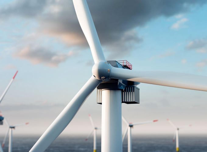 Close-up of a wind turbine with large blades against a cloudy sky, with more turbines visible in the background over the ocean.