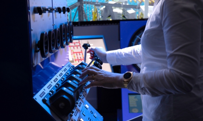 Person operating a control panel with switches and dials, wearing a white long-sleeve shirt and a smartwatch.