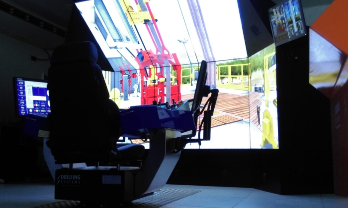 A simulator setup features a large screen displaying equipment, a control chair, and various monitors.