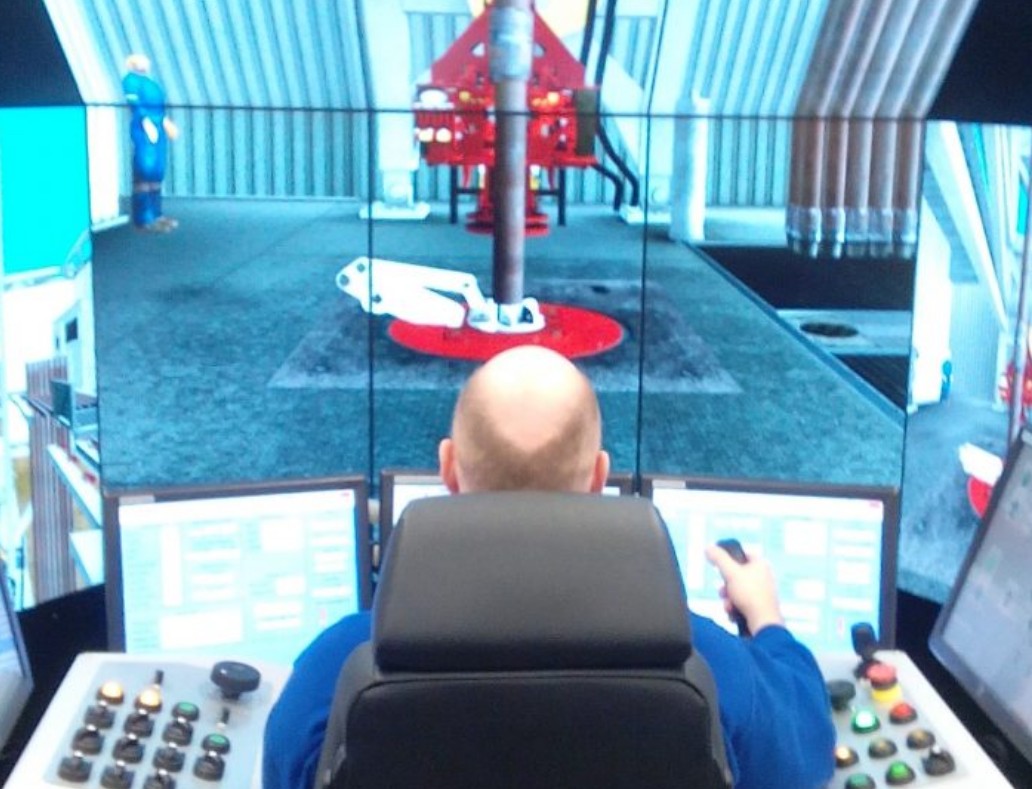 A person operates a control panel with multiple screens displaying an industrial setting, possibly a simulation or monitoring of machinery.
