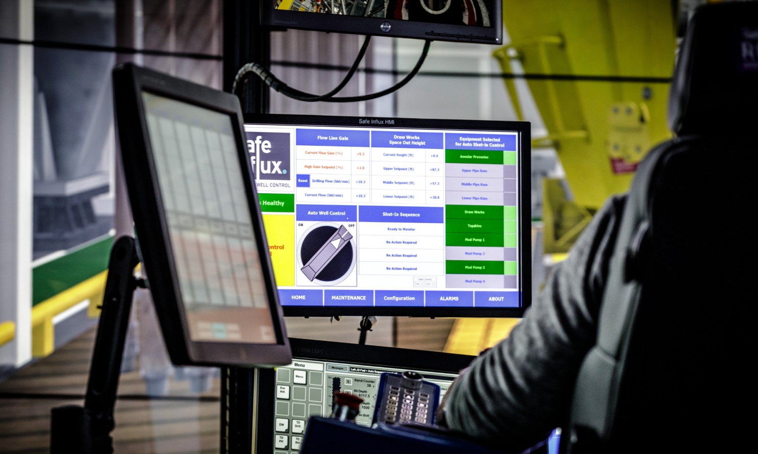 A worker operates machinery using multiple screens displaying data and controls in an industrial setting.
