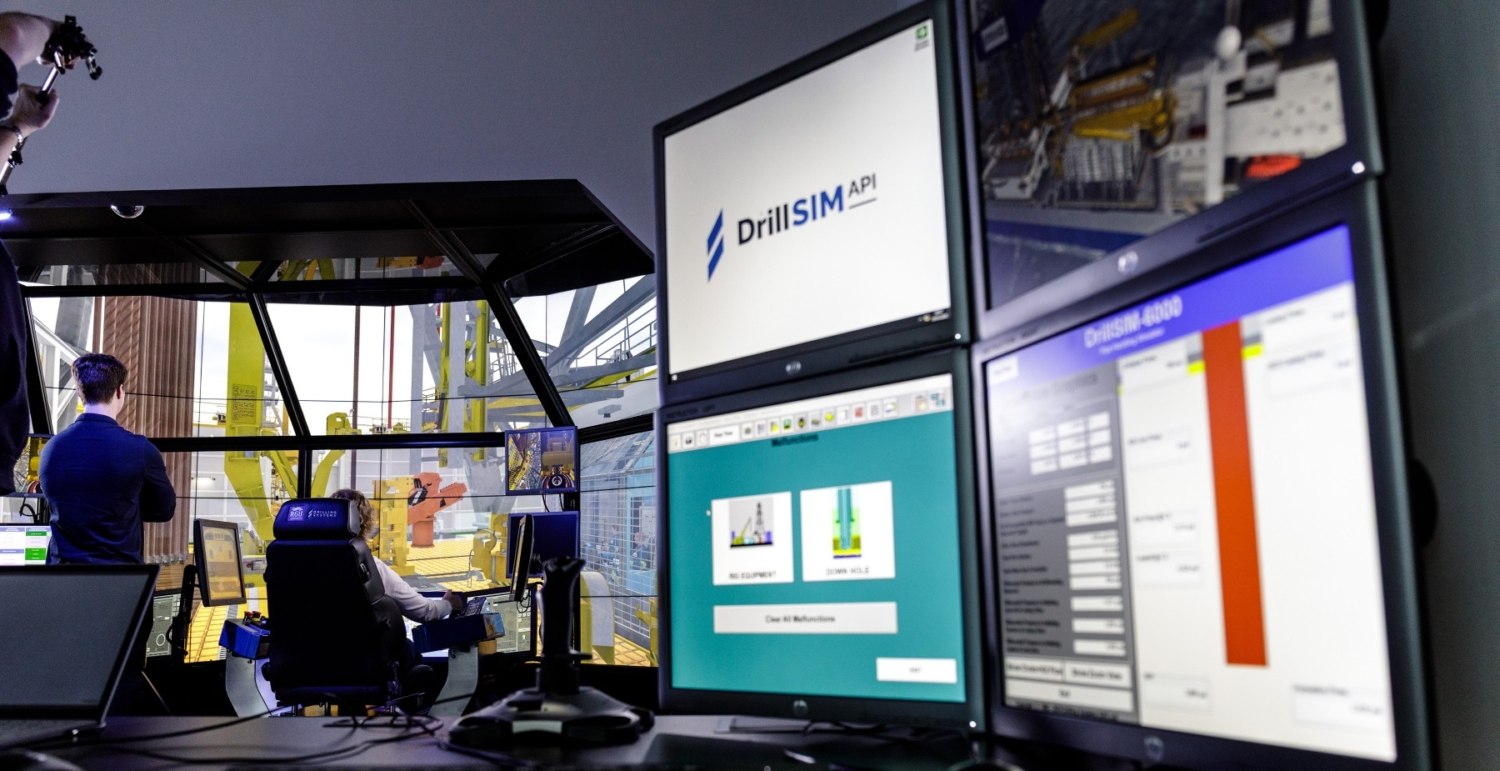 Multiple computer monitors in a control room display simulation software for drilling operations, one screen showing 