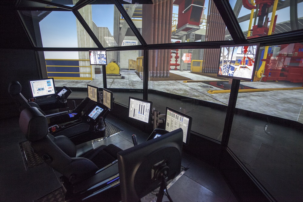 Interior view of a control room with multiple monitors and chairs, featuring screens displaying data and a simulated industrial environment.