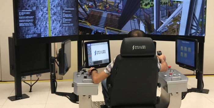 A person operates a high-tech drilling simulation system with multiple screens and control panels, likely used for training or testing purposes.