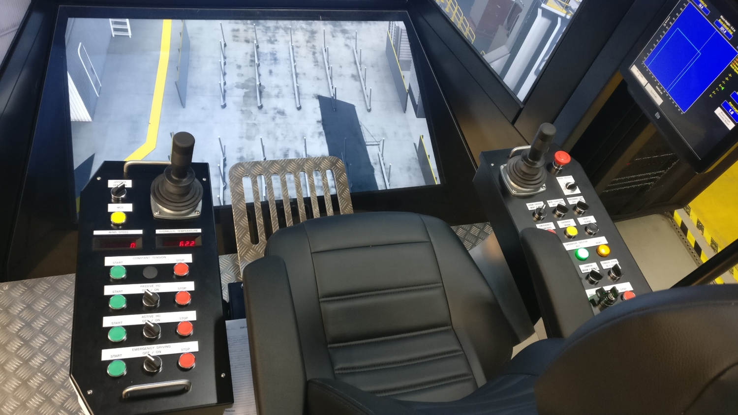 Interior view of a control cabin with two joysticks, multiple buttons, a seat, and a screen displaying equipment data.