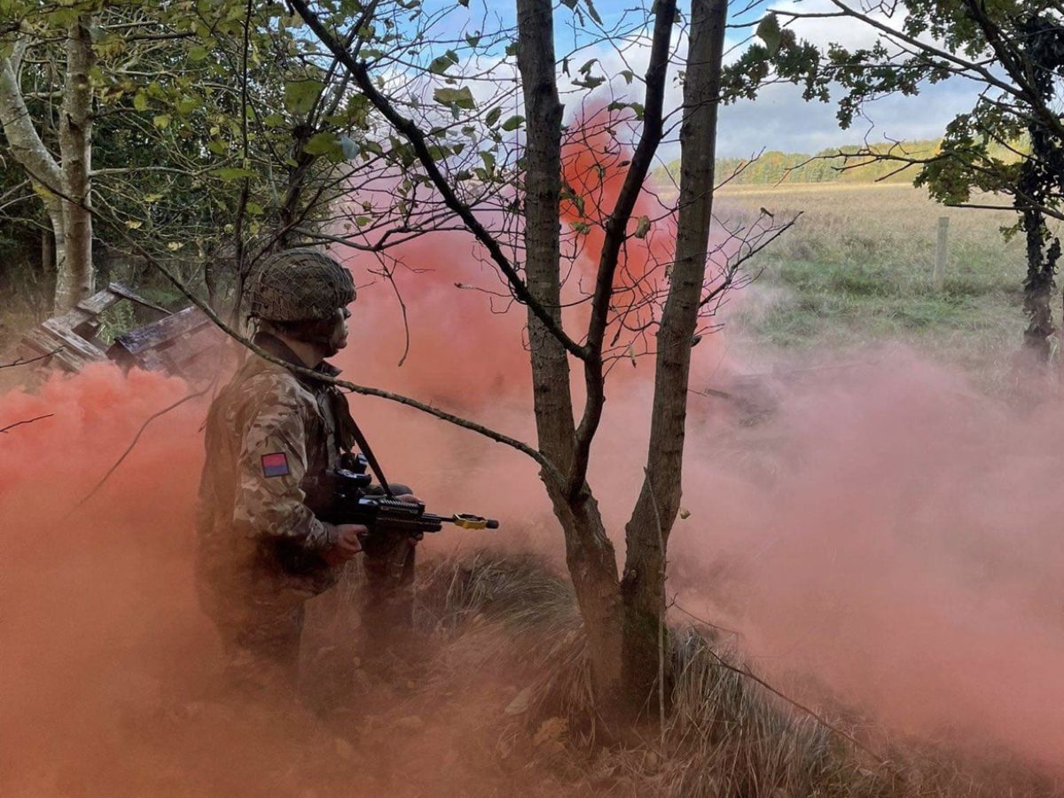 A soldier in camoflage with red smoke.