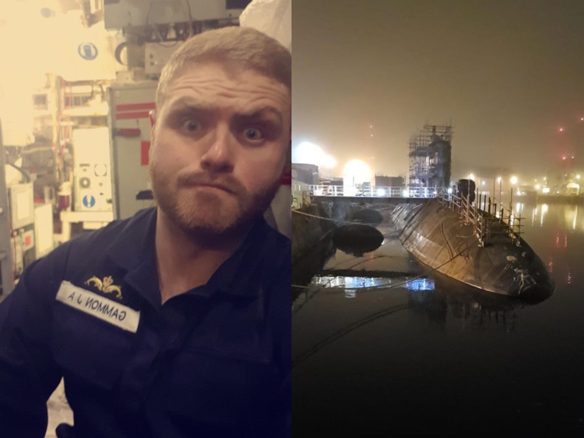 A man in a Navy boiler suit taking a selfie and a submarine in a dock at night, partially submerged