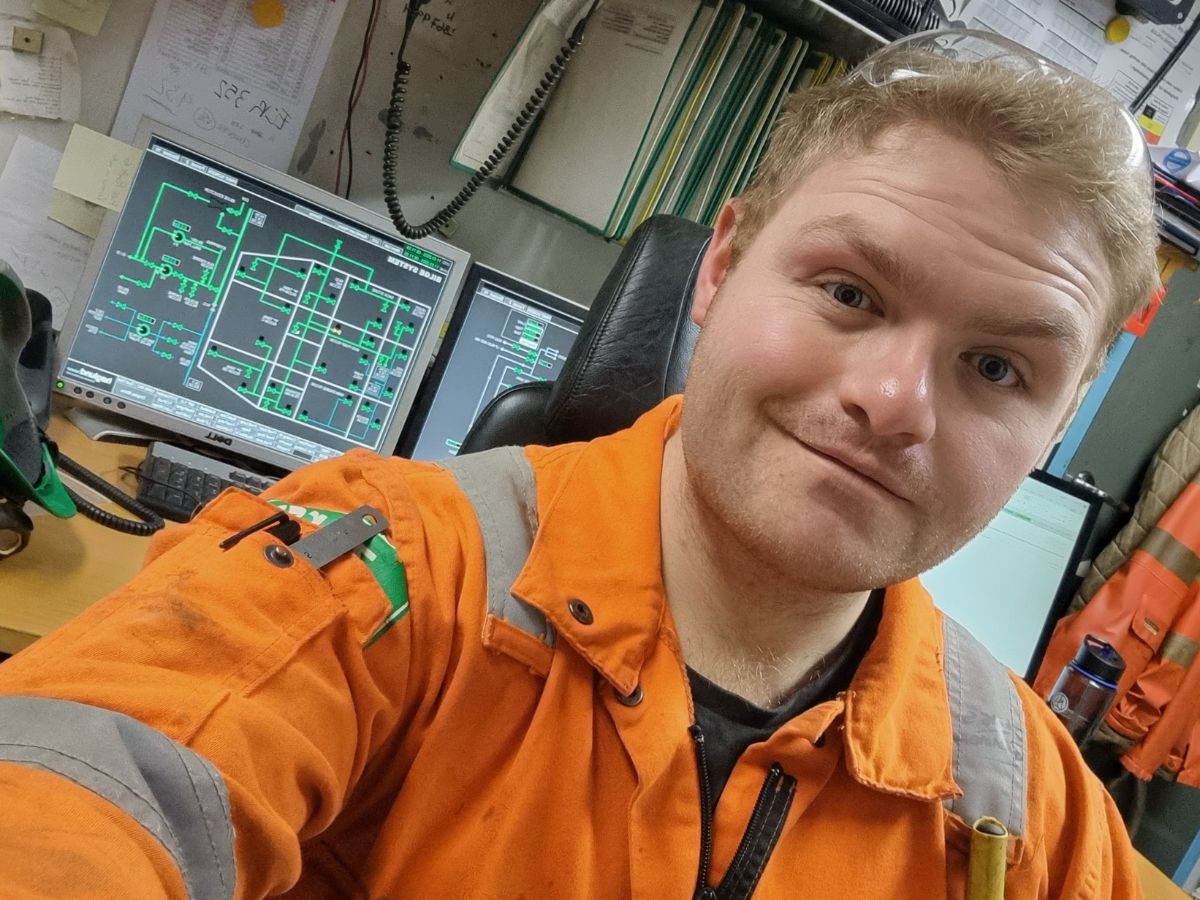 Um homem a tirar uma selfie com um fato de caldeira cor de laranja numa sala de controlo no mar