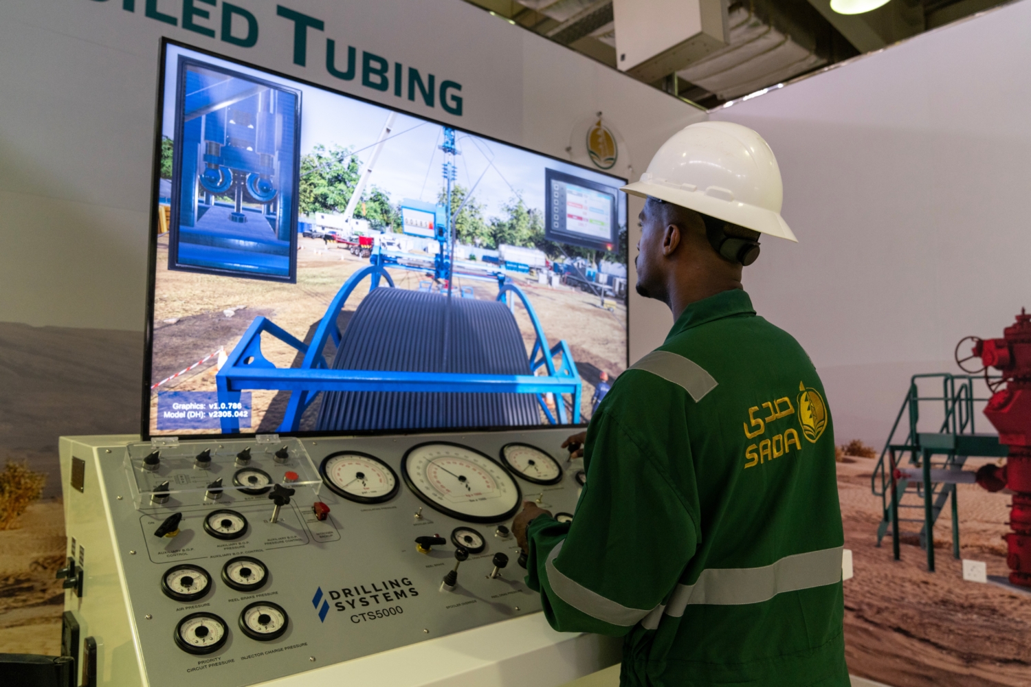 A person in a hard hat operates a sophisticated drilling simulation console with gauges, engaged in an advanced training session, as a large screen vividly displays an oilfield scene.