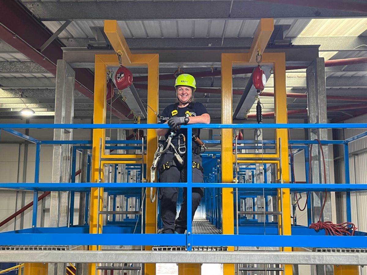 3t instructor with a neon helmet standing on a blue and yellow working at height skills frame. 