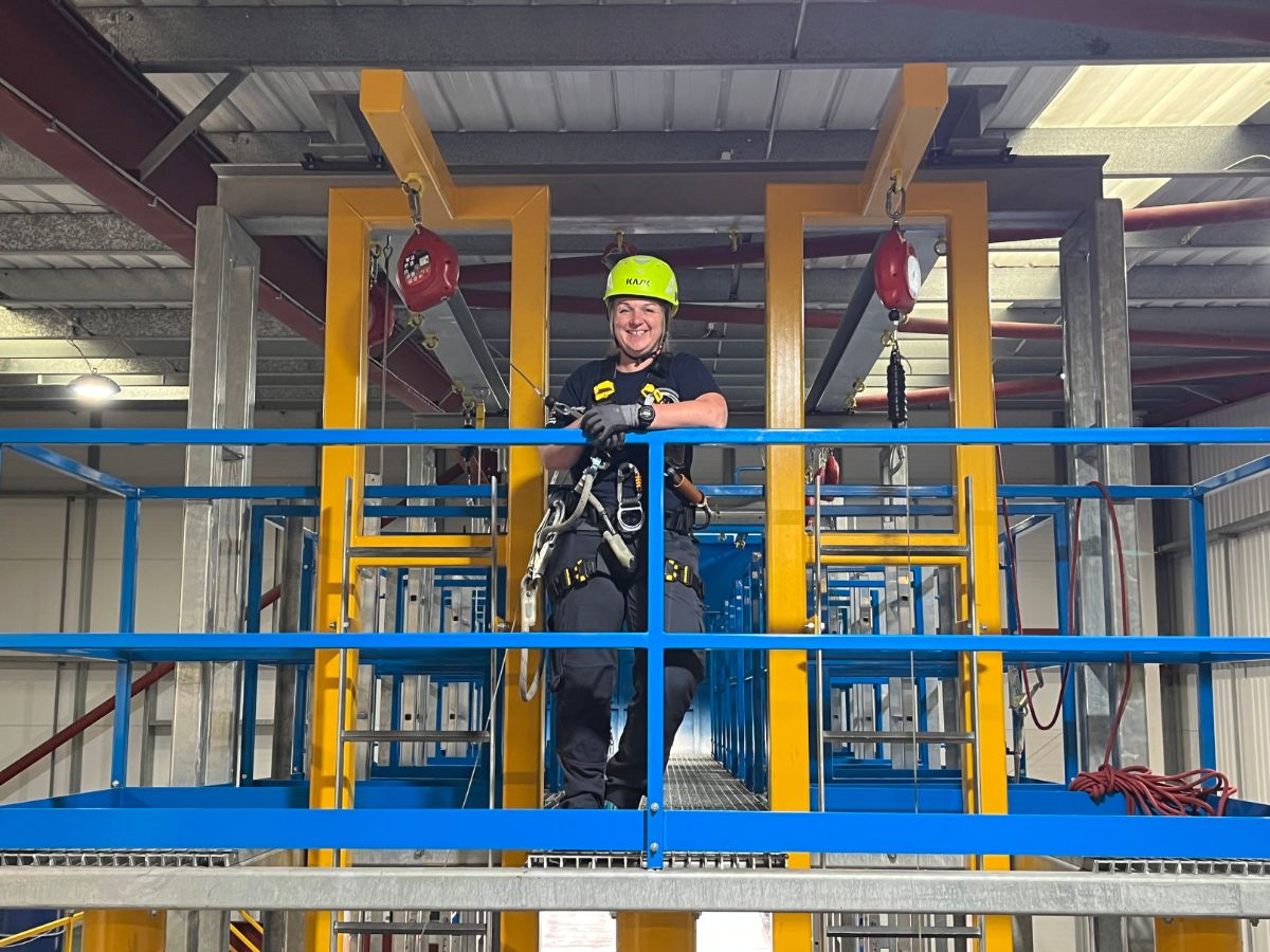 Moniteur 3t avec un casque fluo debout sur un cadre de travail en hauteur bleu et jaune. 