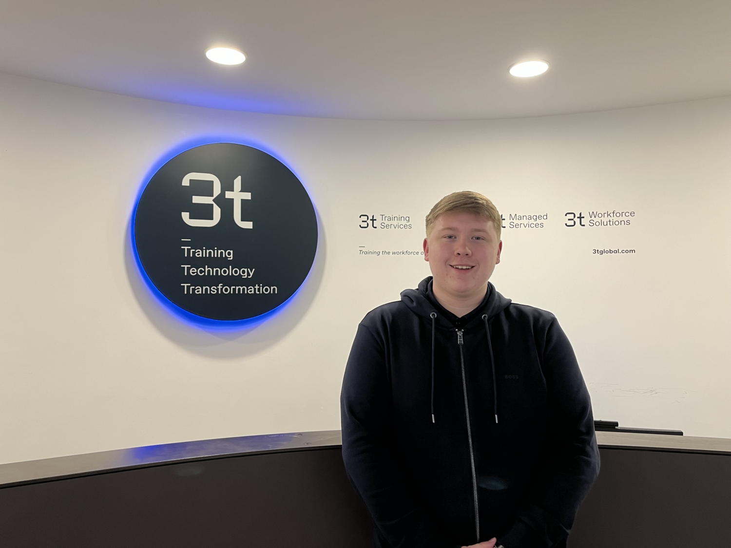 A person stands in front of a reception desk with a sign reading 