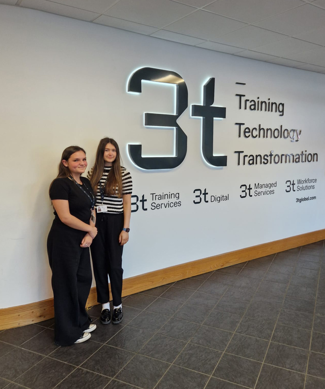 Two people stand in front of a wall adorned with the bold 3t logo and the phrase: 