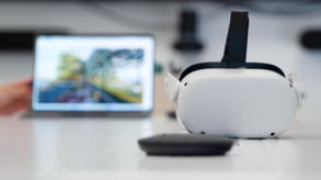 A VR headset and a controller are placed on the table in front of a blurred laptop displaying a landscape image, creating an immersive atmosphere that hints at virtual training possibilities.
