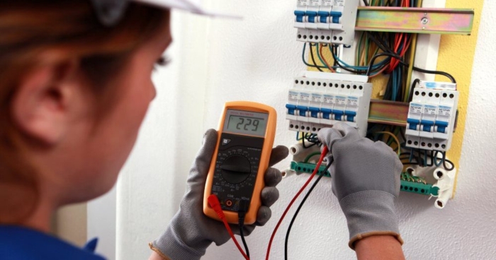 Person using a multimeter to test voltage in an electrical panel.