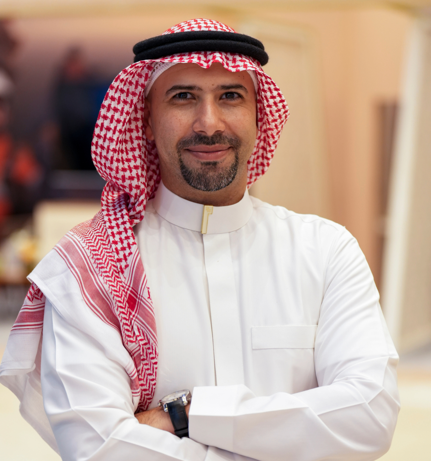 Man with a beard wearing a white thobe and a red and white keffiyeh, smiling with arms crossed.
