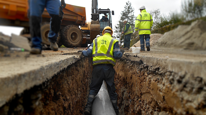 Men wearing yellow high vis jackets laying pipework in a street trench